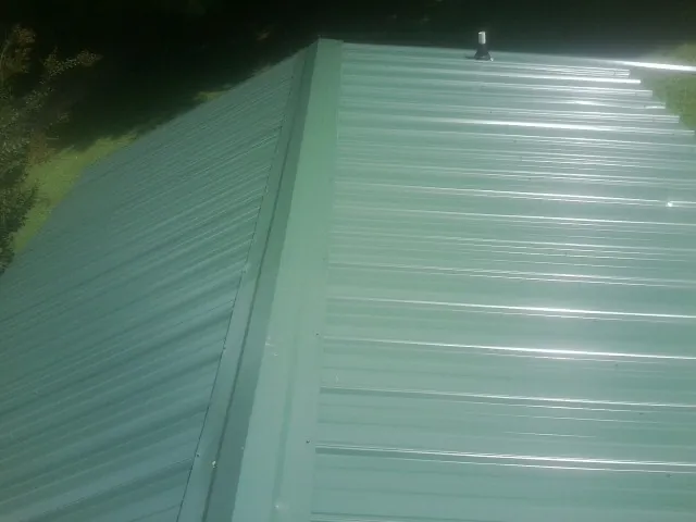 New green metal panels meeting at the ridge of a roof — Flat Roof Repair work by our crew in Gadsden