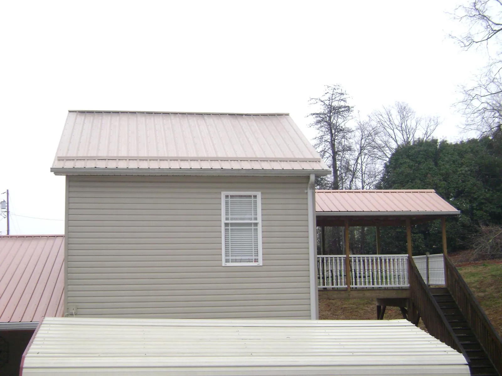Tan metal roofs on a two story addition and attached porch, from a Roof Replacement job in Gadsden